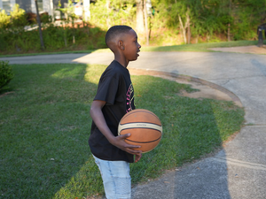 a young boy holding a basketball on a street