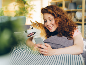 a woman laying on a bed with a dog looking at a cell phone