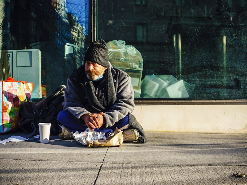 man in black and gray jacket sitting on sidewalk during daytime