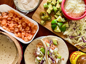 Delicious grilled shrimp taco dinner with slaw, limes, avocados, jalepenos, tartar sauce, flour tortillas, grated cheese, and salsa ready for family dinner.