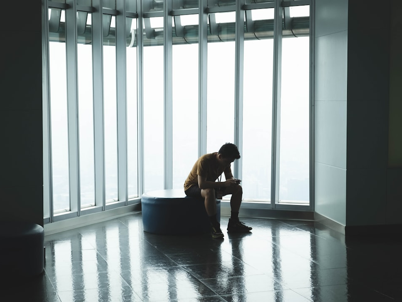 man sitting on ottoman chair near window