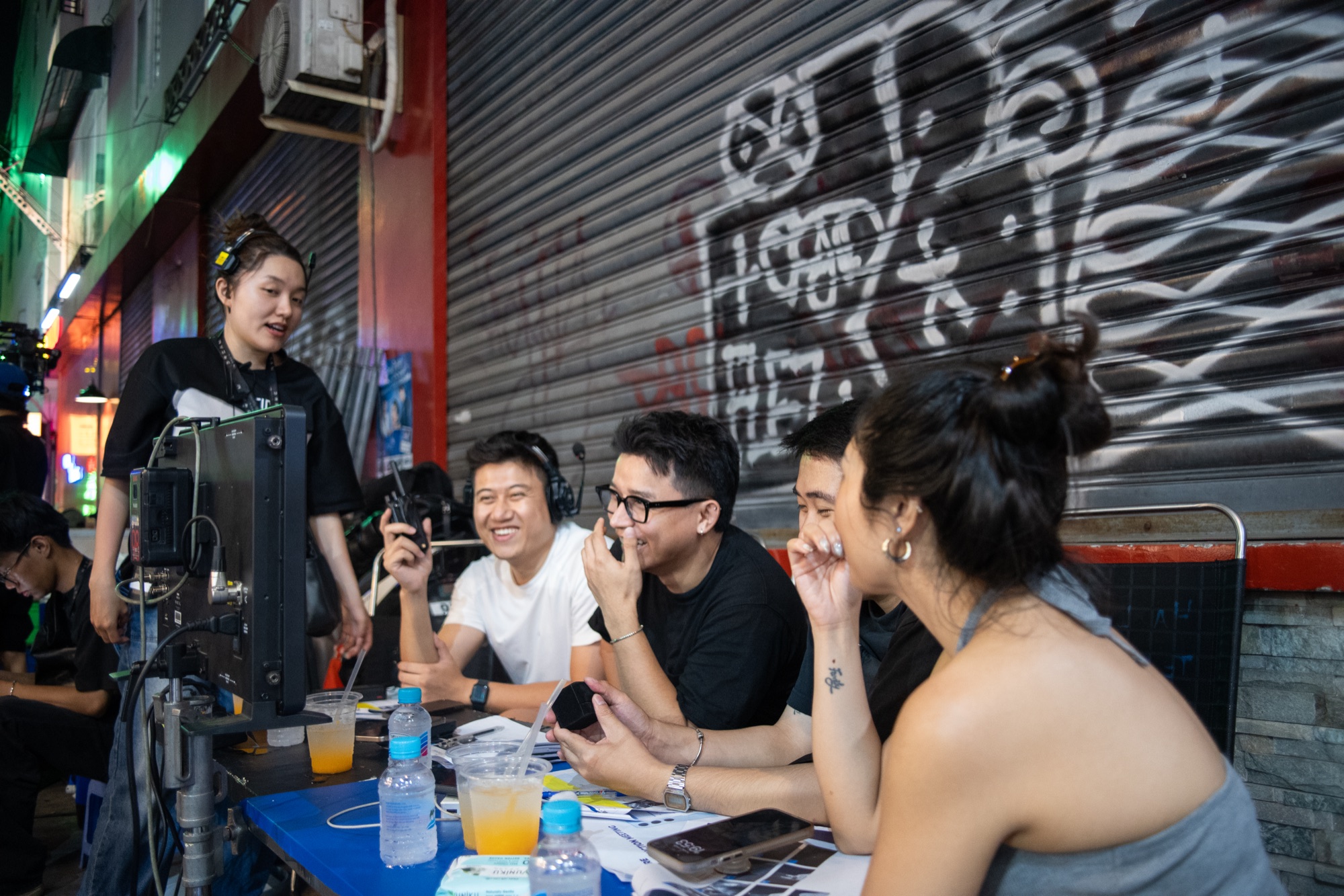 Crew and cast at a monitor and a folding table on the pavement in front of a graffitied shop shutter during a Samsung Galaxy S24 night shoot