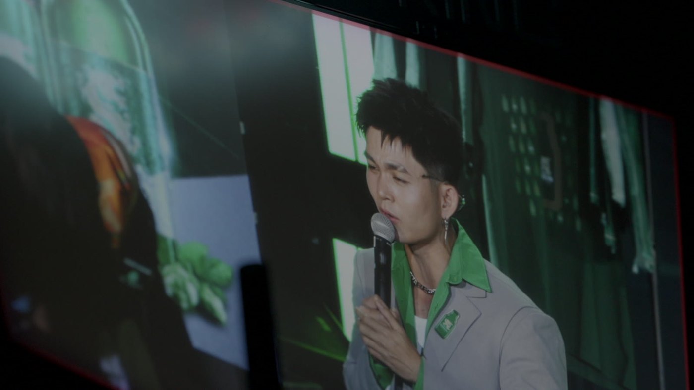 A host with a microphone shown on the large venue screen during a brand live show