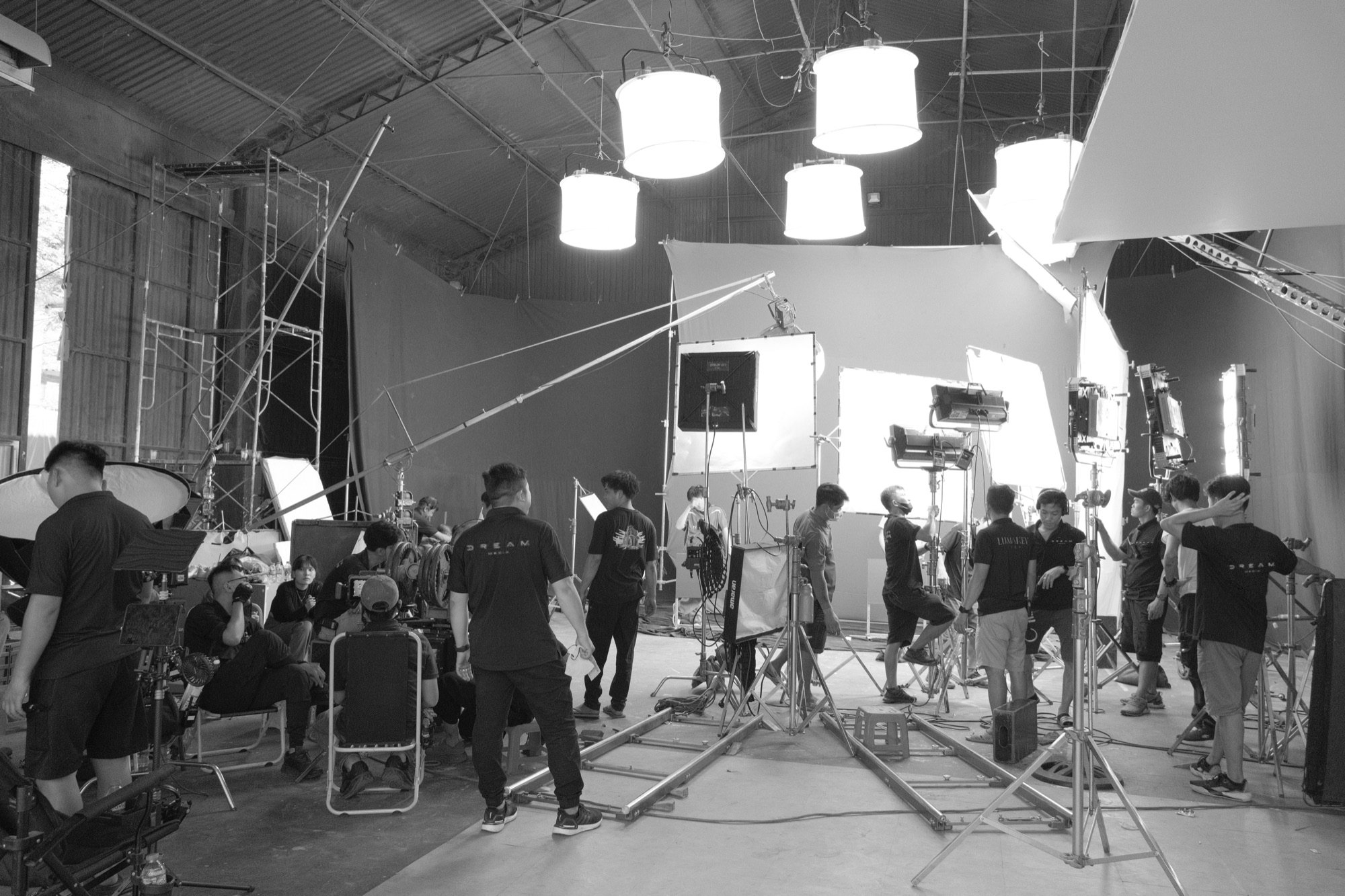 Black-and-white view of a large studio with green and blue screens, overhead lights, a camera jib and a full film crew during a CeraVe shoot