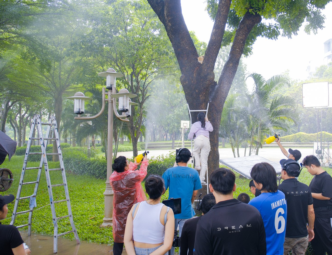 Crew on ladders holding rain pipes over a park path, with hoses and pump on the grass, during a Samsung Galaxy A shoot