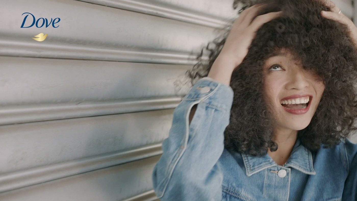 A woman with curly hair laughing in a frame from a Dove hair bumper