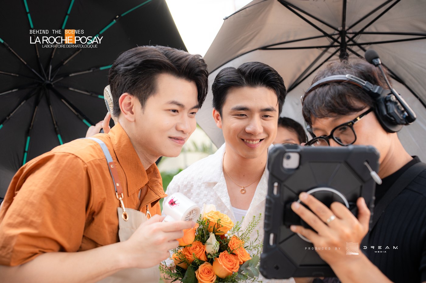 Two actors and a crew member smiling over playback on a tablet during a La Roche-Posay shoot