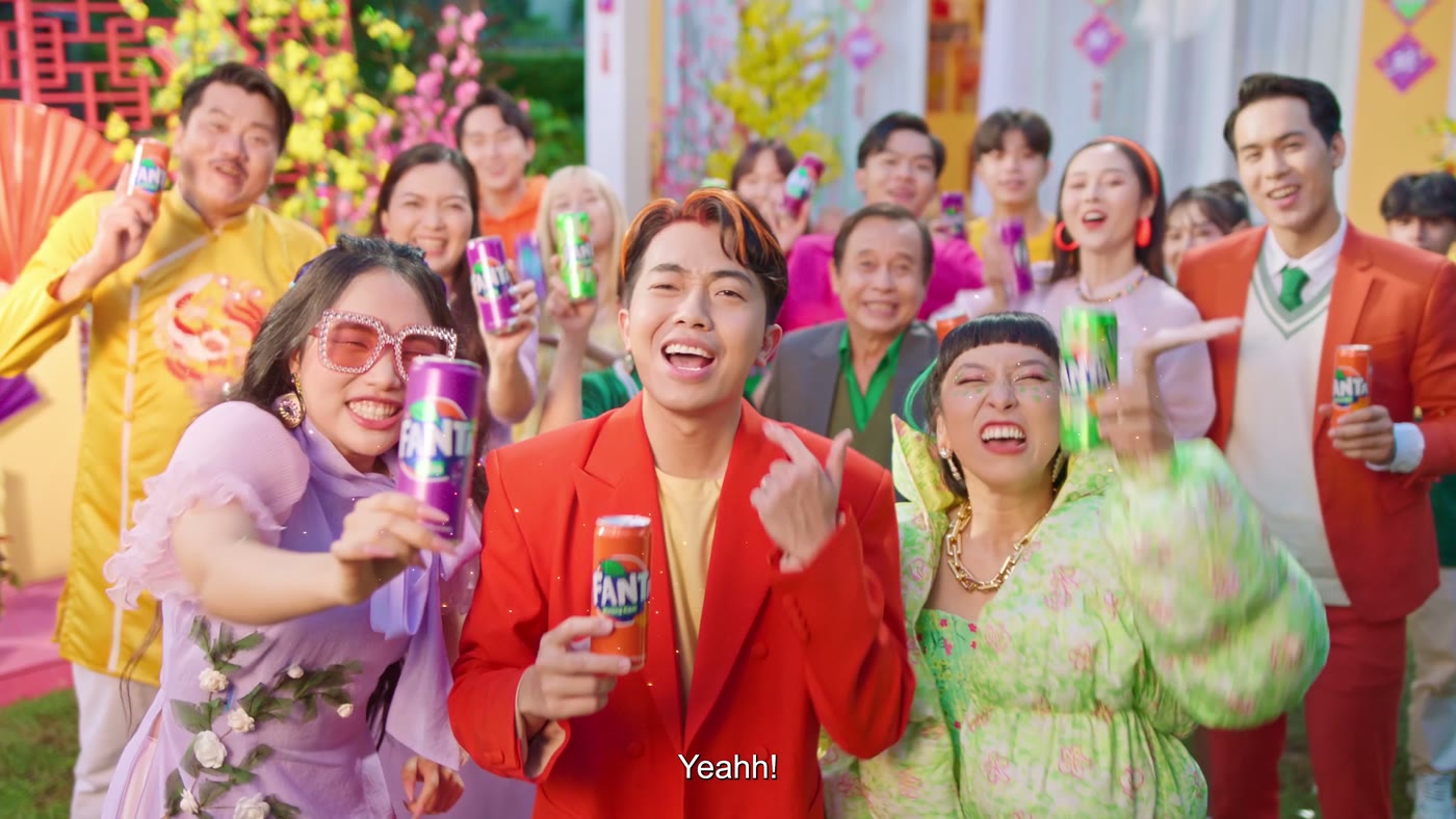The whole cast of a Fanta Tết commercial singing and raising cans of Fanta in a garden dressed for Tết