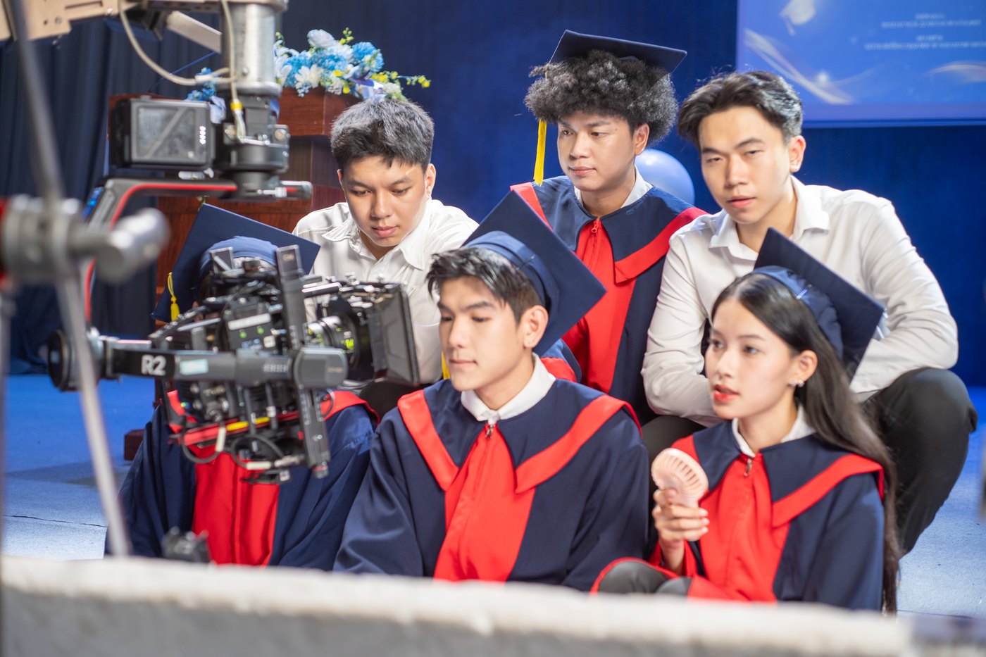 Cast in graduation gowns checking a take on a camera monitor with the crew on a Samsung Galaxy A56 shoot