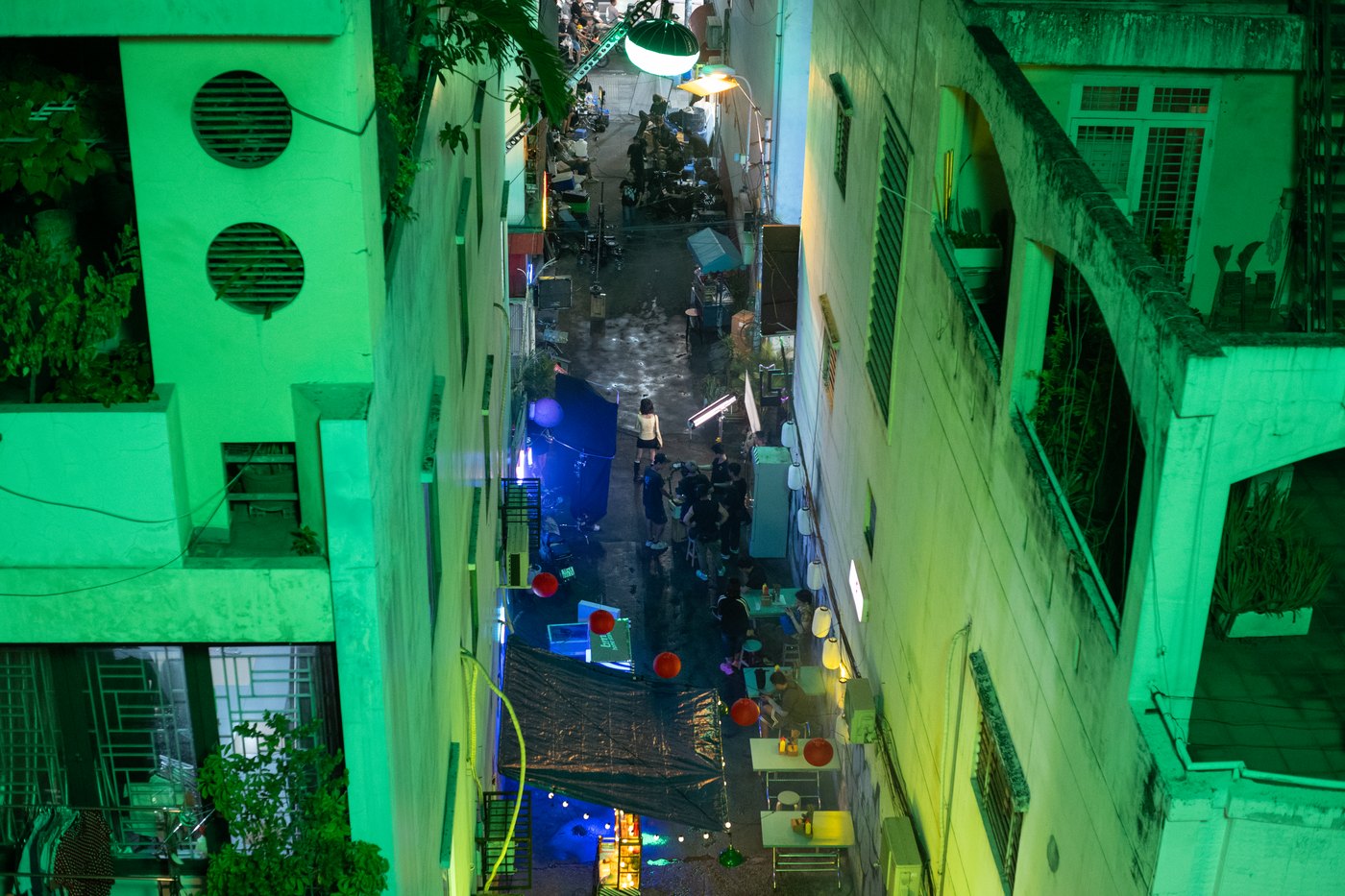 Aerial view of a narrow alley dressed with lanterns and street tables and lit green for a Samsung Galaxy S24 night shoot