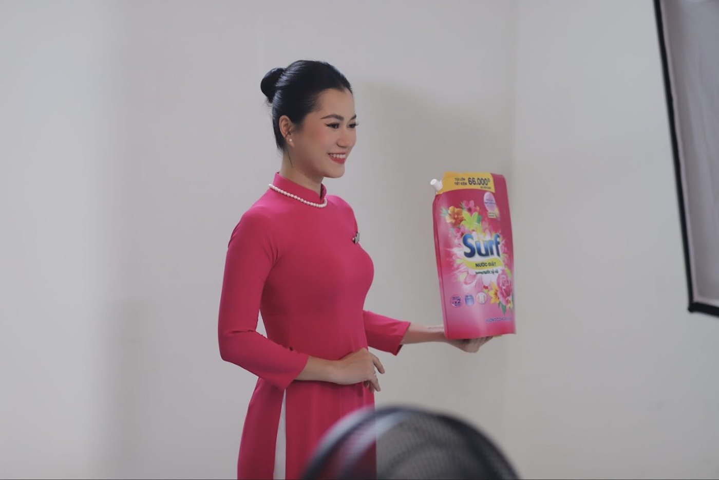 Actress in a pink áo dài holding a Surf detergent pack for the camera