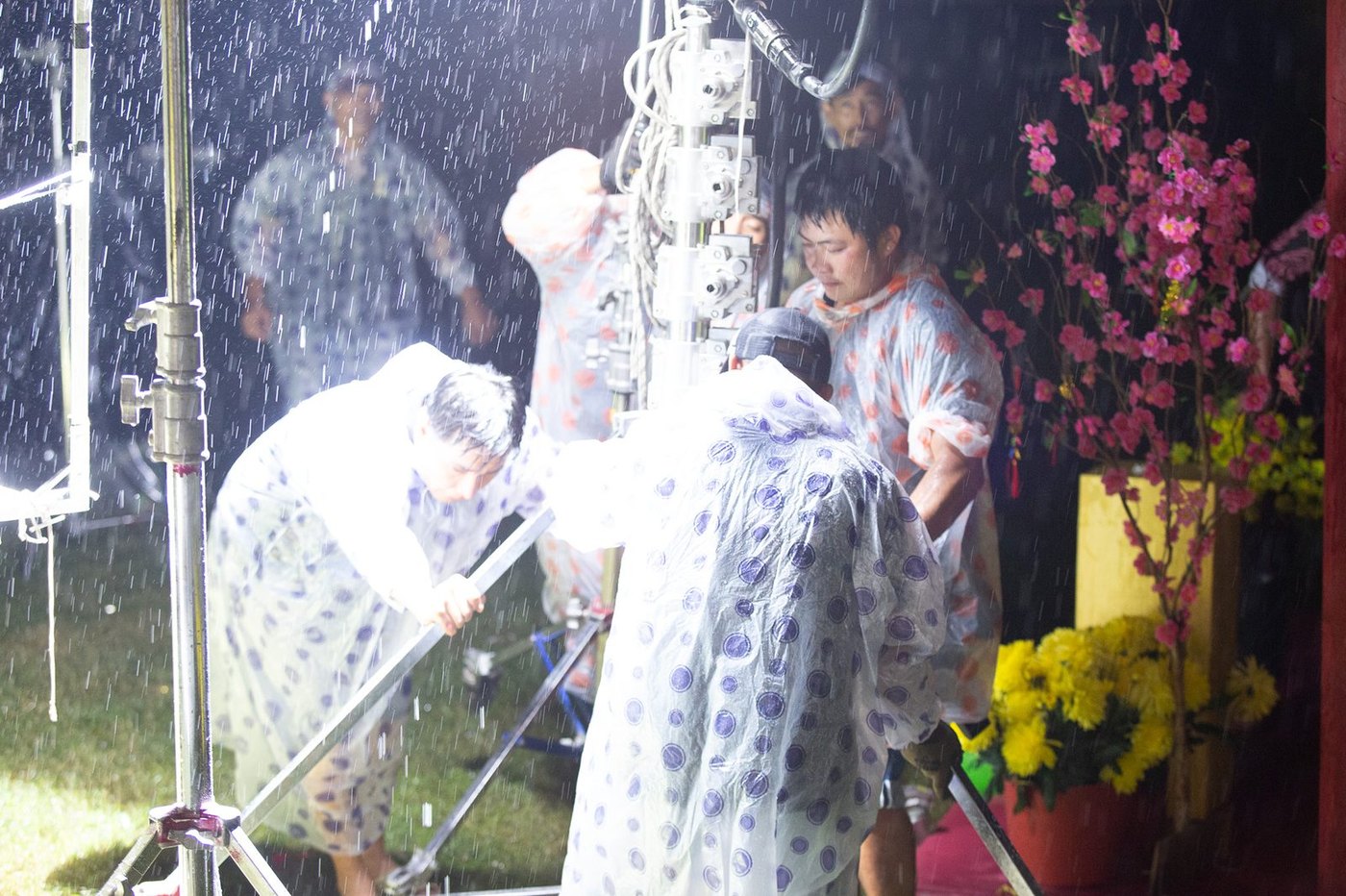 Rain machine running over actors in raincoats on a Tết film set for Fanta