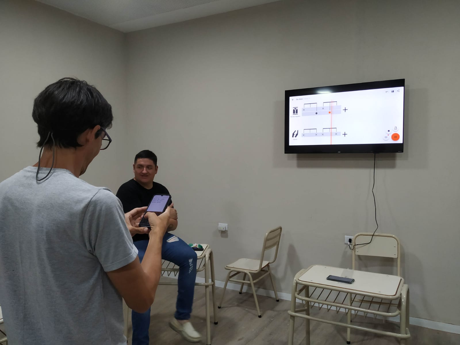 Teacher using Drum Notes app on phone to display notation on a TV screen in classroom