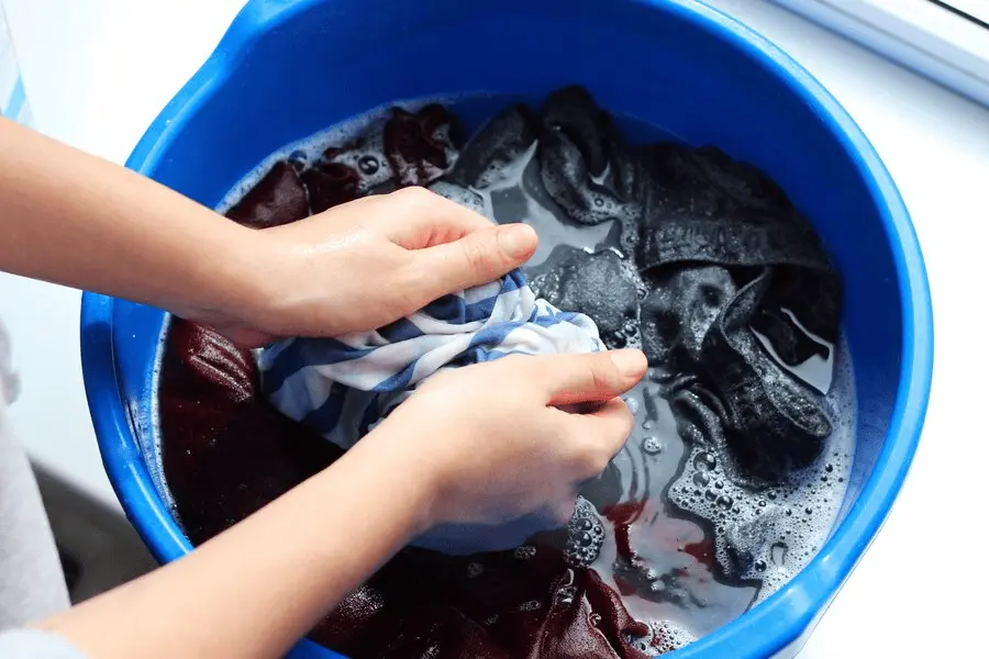 A person hand washing clothes in a bucket