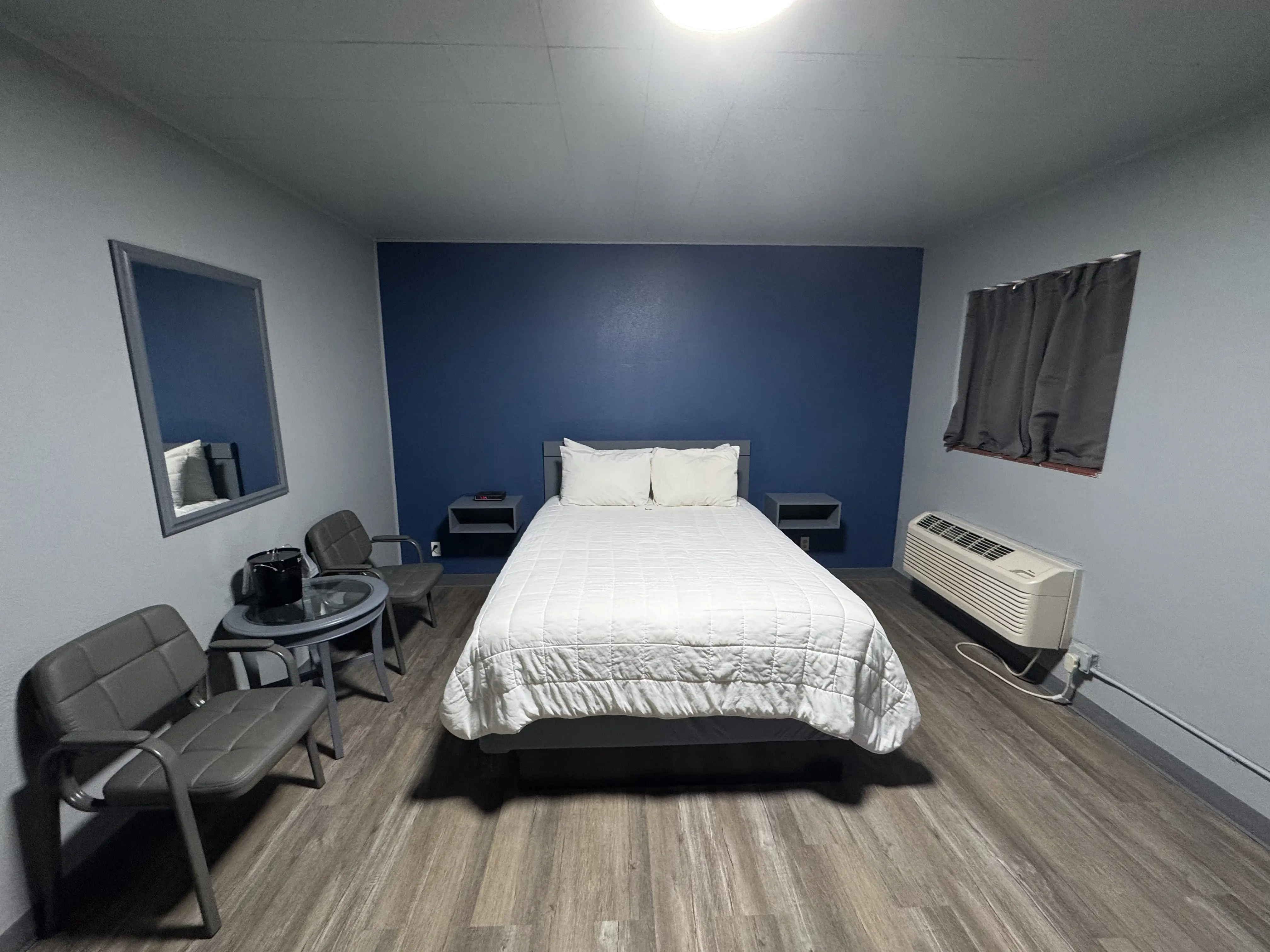 Renovated modern hotel room interior featuring a blue accent wall, queen bed, and seating area. Part of our inclusive rental packages in Waynoka, Oklahoma, located near Little Sahara State Park.