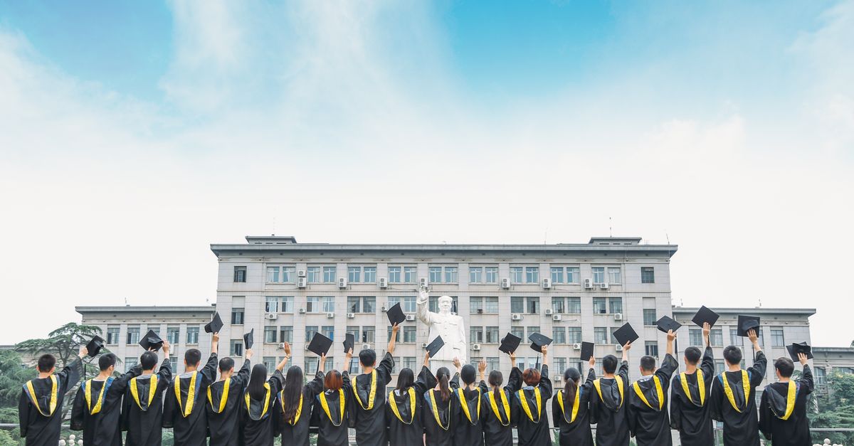 Group of graduates in gowns celebrating outdoors with a building backdrop.