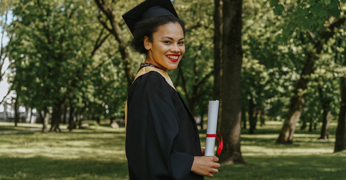 Smiling graduate holding diploma in a park setting