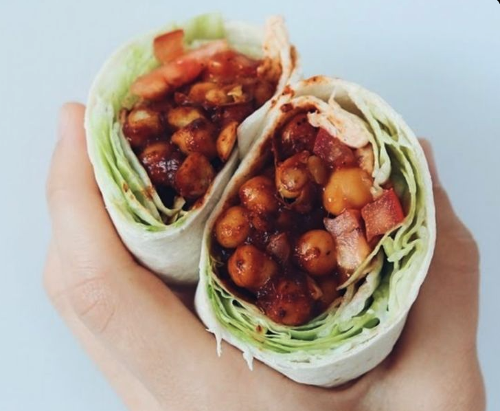 Two halves of a stuffed wrap on a plate showing a cross-section of smoky BBQ chickpeas, creamy avocado, crunchy slaw, and pickled jalapenos.