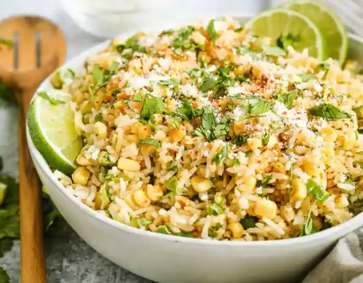 A vibrant bowl of white rice topped with charred golden corn, black beans, flecks of red spice, and bright green cilantro.