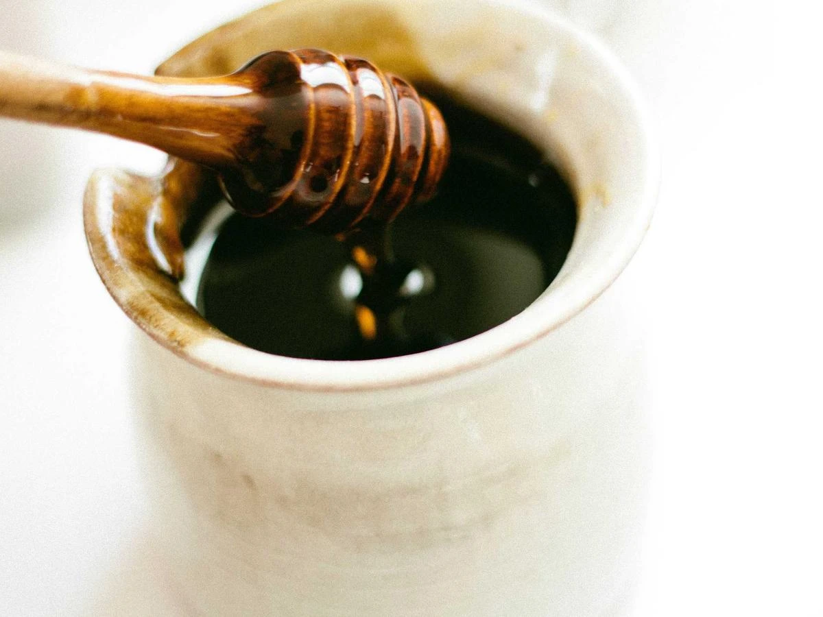 Raw honey dripping from a wooden dipper into a jar