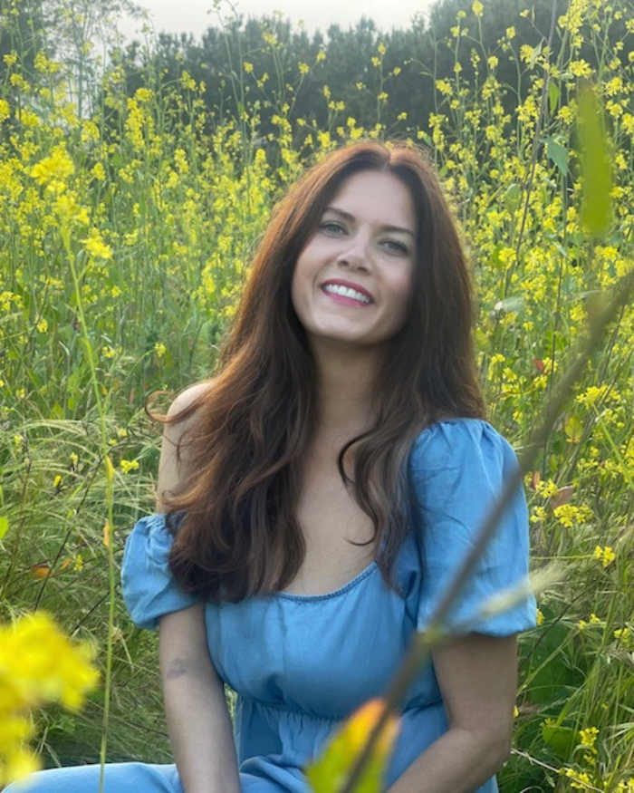 Danielle, a professional cuddler in Carlsbad, smiling in a field of yellow wildflowers