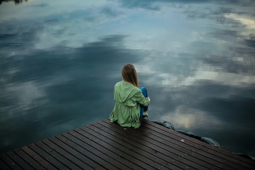 Person sitting on a dock overlooking calm water