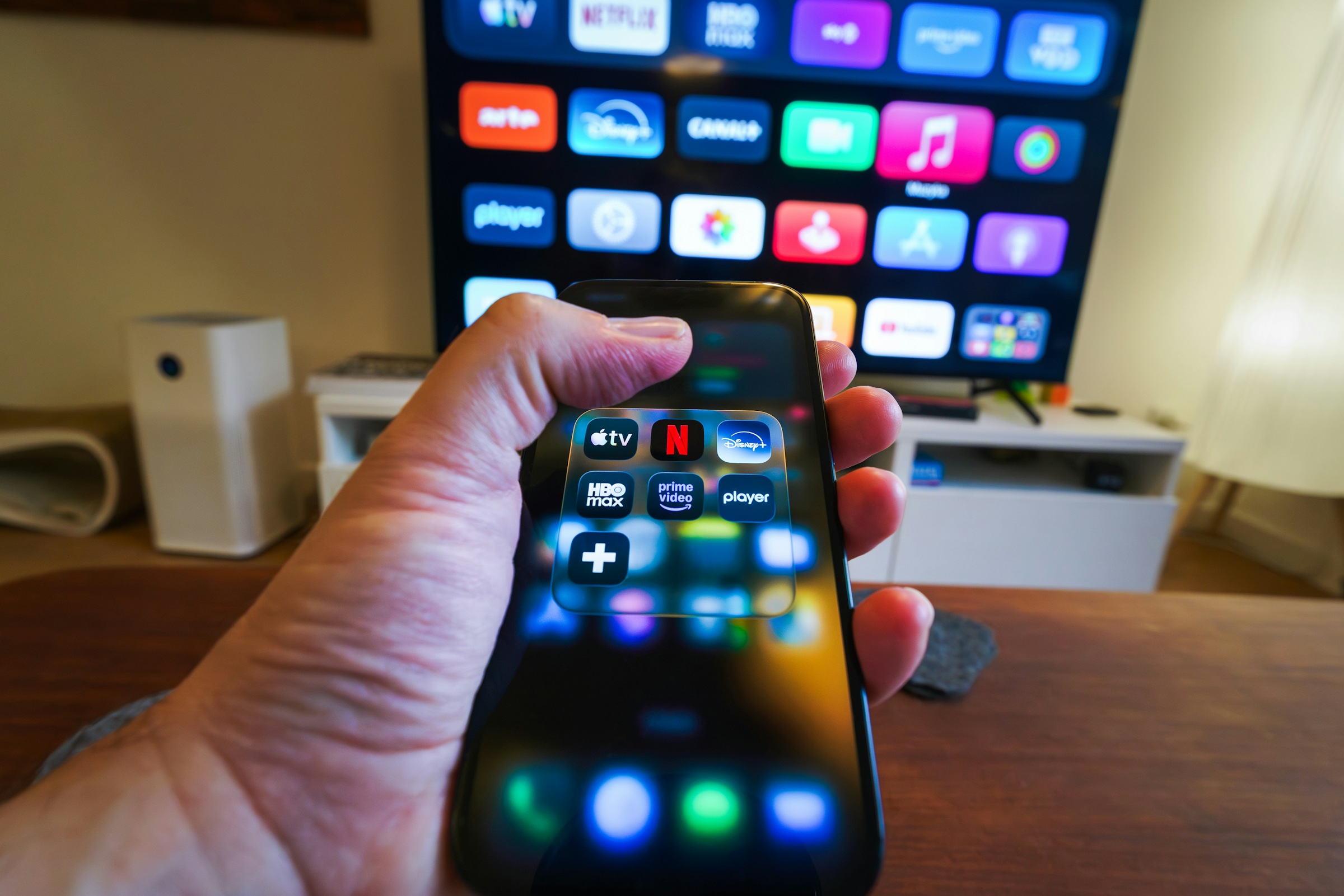 Hand holding smartphone controlling smart TV apps
