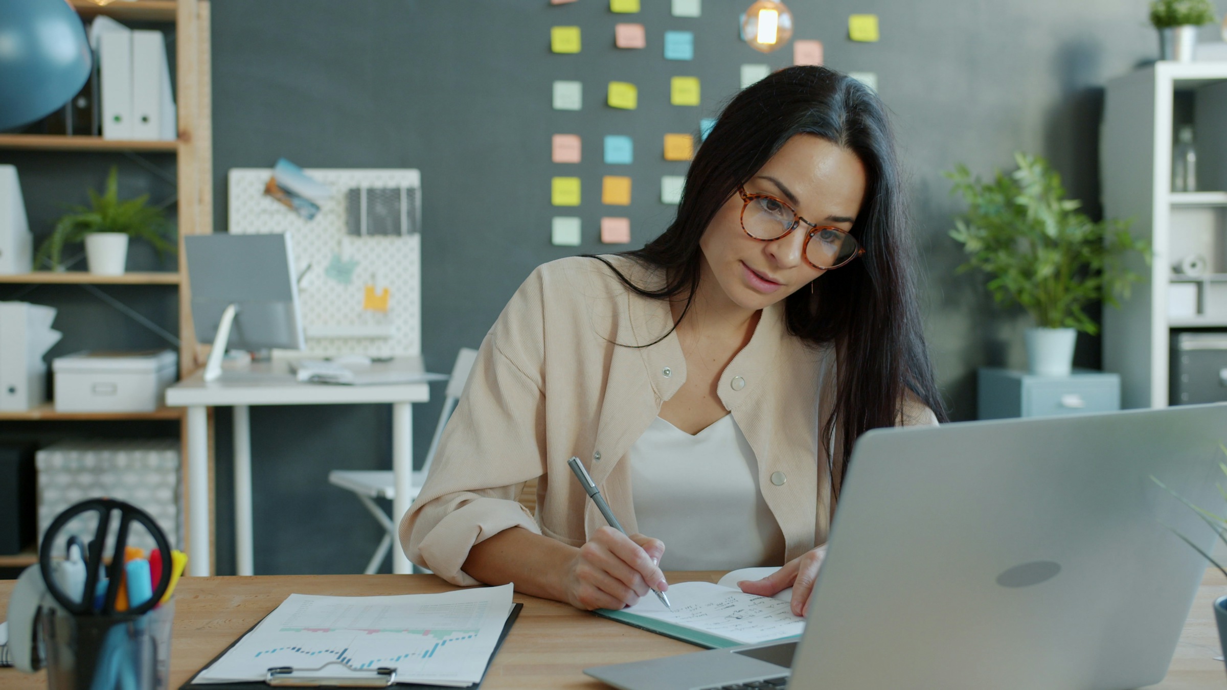 Woman working at a desk with laptop and notebook.