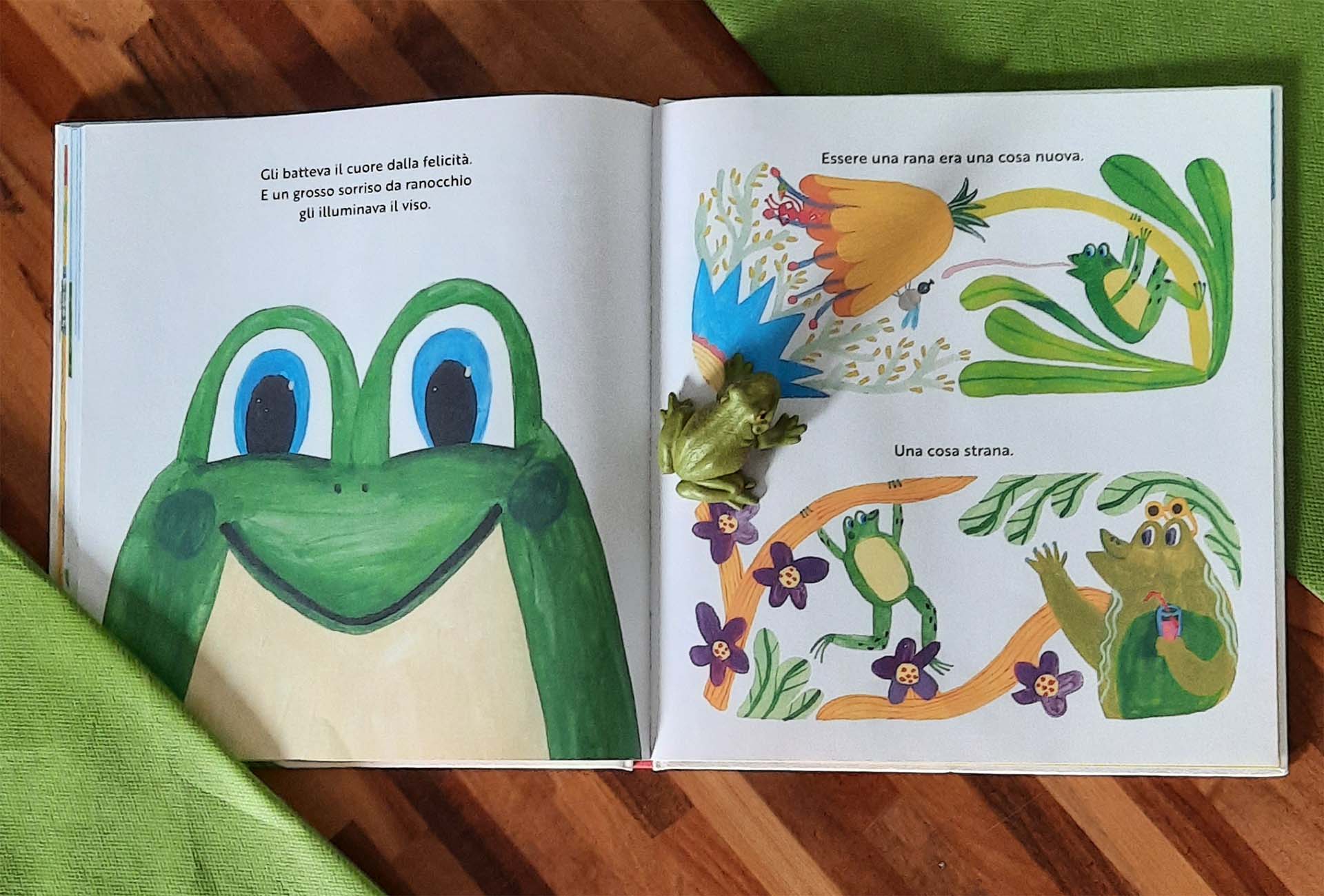 Doppia pagina: a sinistra il muso di una rana verde con un grande sorriso occupa tutta la pagina, a destra piccole rane fra i fiori viola, una cattura un insetto con la lingua