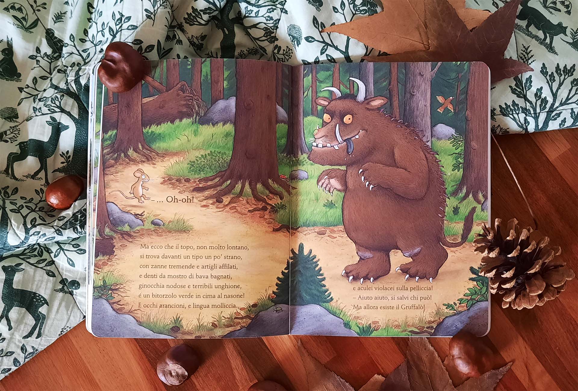 Doppia pagina: a sinistra il topolino minuscolo sul sentiero esclama «Oh-oh!» e sotto corrono i versi che descrivono il mostro, a destra il Gruffalò a figura intera, occhi arancioni, zanne, lingua fuori e aculei lungo la schiena