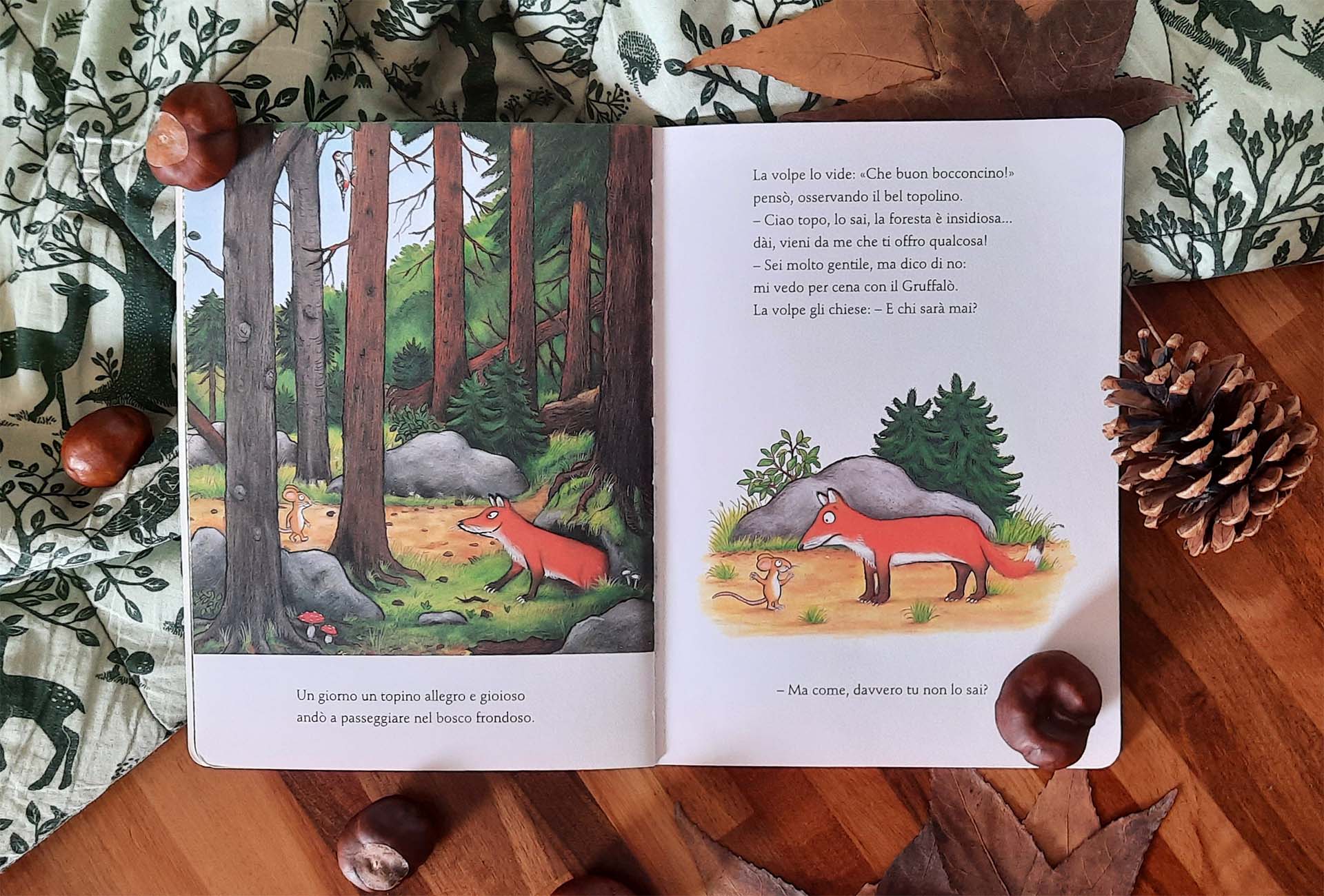 Doppia pagina: a sinistra il topolino cammina in un bosco di tronchi alti e la volpe lo osserva da dietro un masso, a destra i due sono uno di fronte all'altro su una striscia di terra chiara, con il testo del dialogo sopra