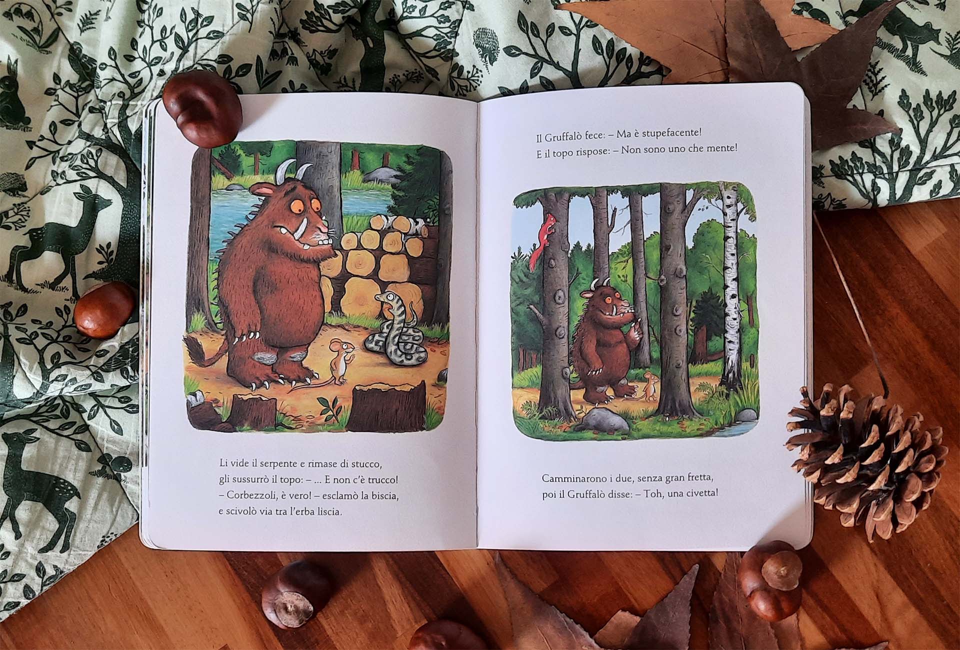 Doppia pagina: a sinistra il Gruffalò e il topolino davanti a una biscia arrotolata accanto a una catasta di tronchi, a destra i due camminano fra gli alberi, il mostro davanti e il topo piccolissimo di fianco