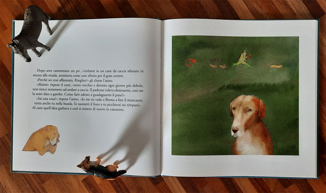 Doppia pagina: a sinistra il testo dell'incontro fra l'asino e il cane da caccia, a destra il cane anziano ritratto in primo piano su un prato verde, con sopra di lui piccole vignette che mostrano un corno da caccia, due lepri, il cacciatore che corre e un cane giovane che salta