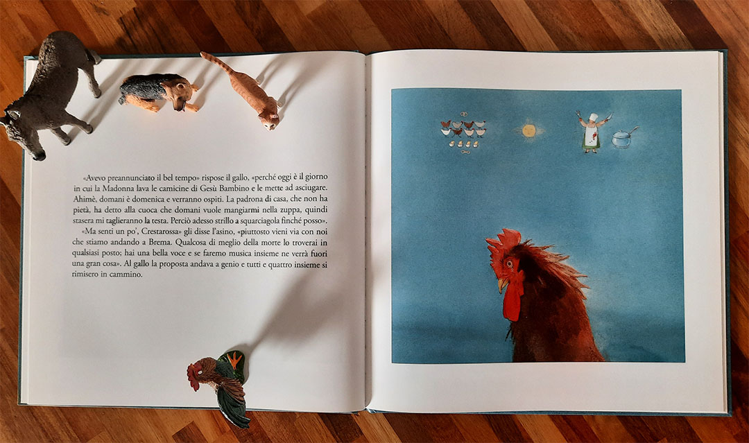 Doppia pagina: a sinistra il testo con la risposta del gallo sulla Madonna che lava le camicine di Gesù Bambino, a destra il gallo in primo piano su fondo azzurro, sormontato da piccole vignette con delle galline, il sole, la cuoca a braccia alzate e una pentola