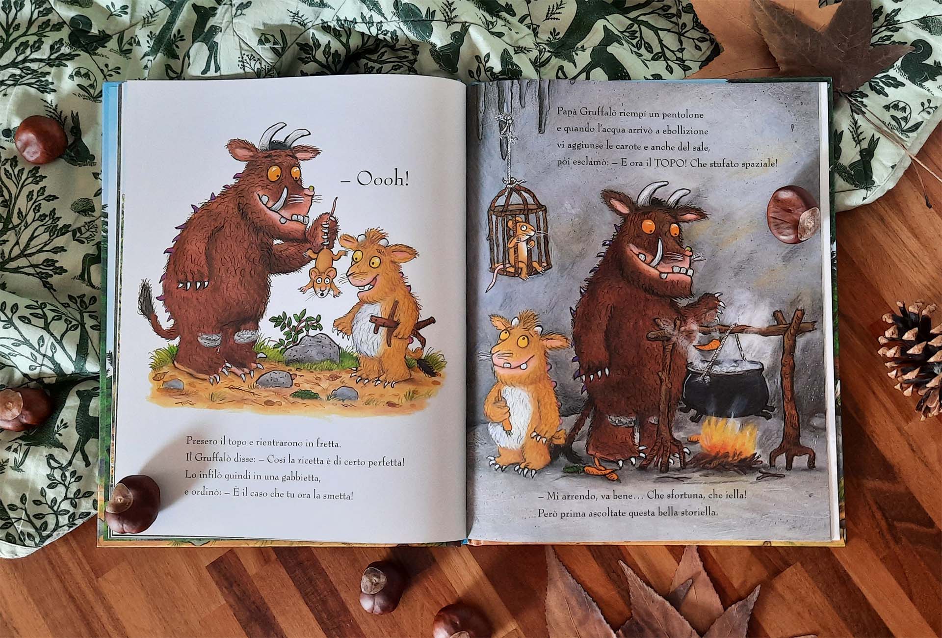 Doppia pagina: a sinistra il Gruffalò tiene il topolino per la collottola davanti alla piccolina, a destra la caverna con il pentolone sul fuoco e il topo chiuso in una gabbietta appesa