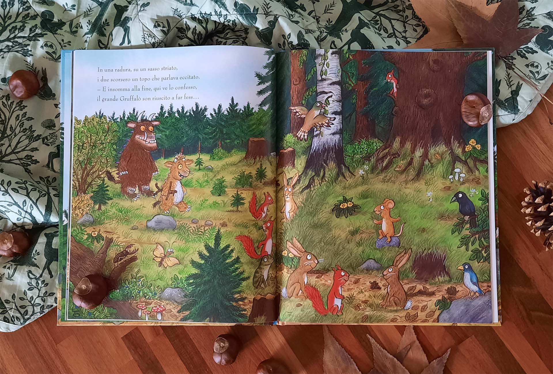 Doppia pagina: a sinistra il Gruffalò e la piccolina attraversano una radura, a destra il topolino in piedi su un sasso parla a scoiattoli, conigli, uccelli e una rana