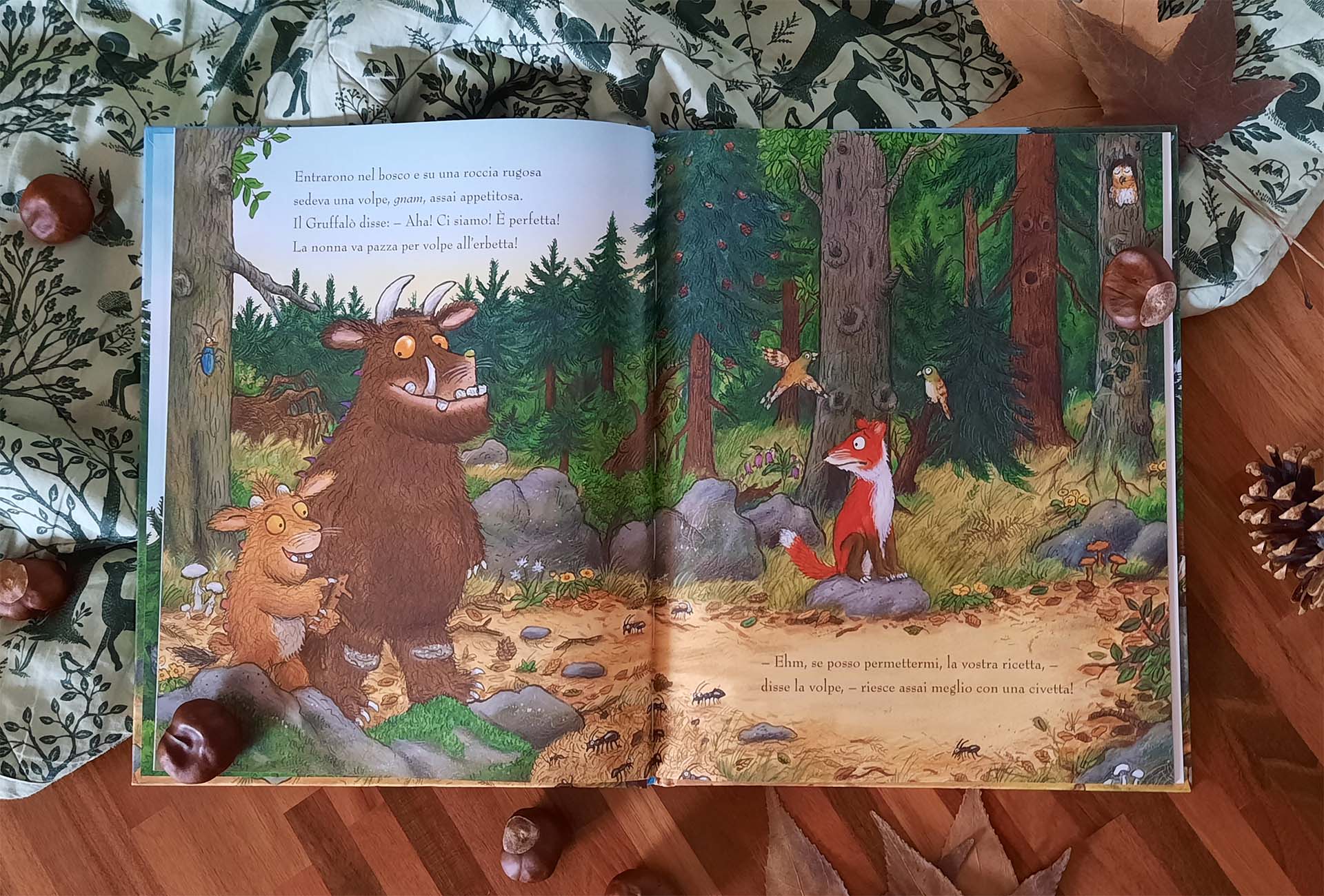 Doppia pagina nel bosco: a sinistra il Gruffalò e la piccolina osservano una volpe, a destra la volpe in piedi fra i tronchi parla indicando altrove