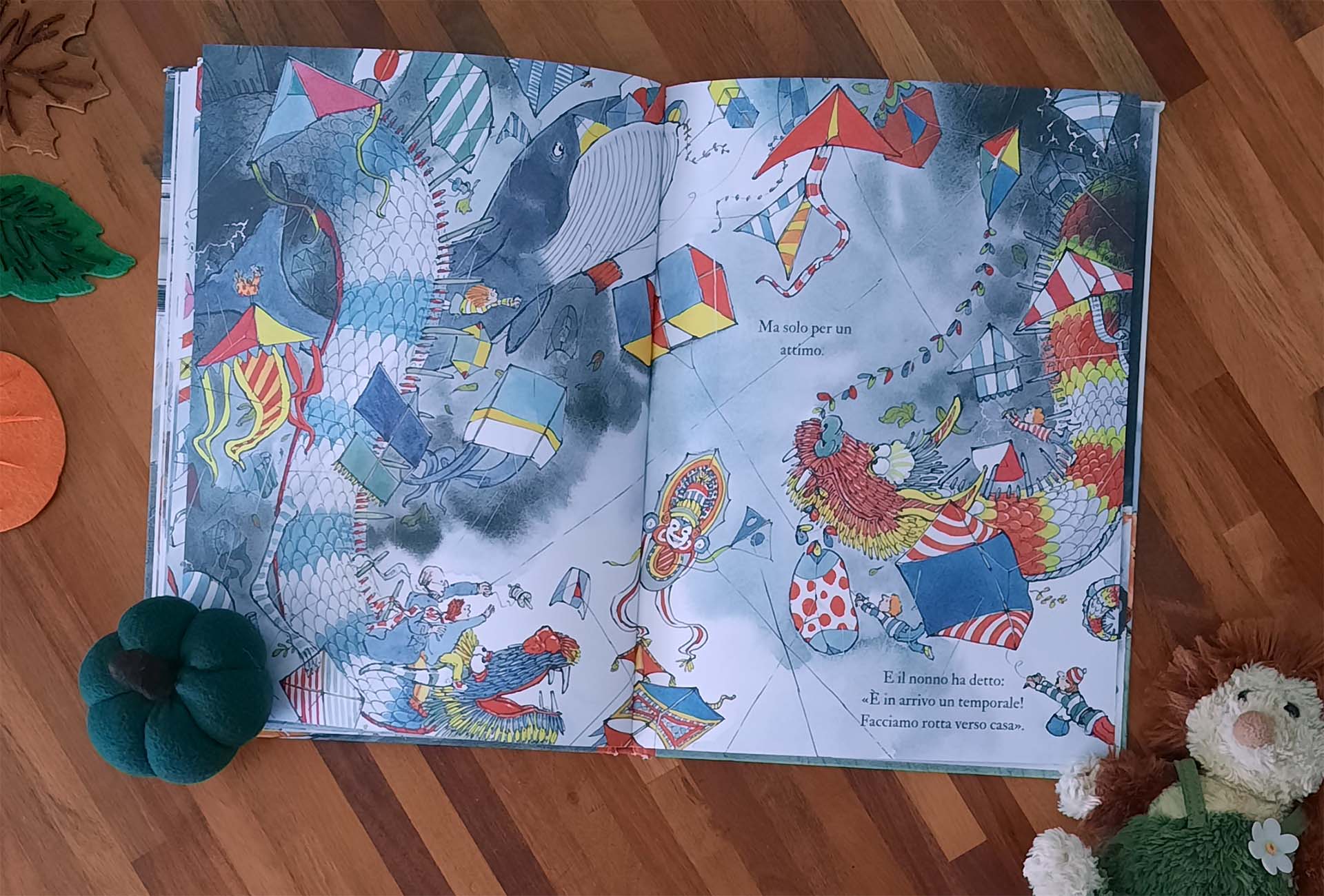 Doppia pagina fra le nuvole: decine di aquiloni giganti a forma di drago, balena e pagliaccio riempiono un cielo grigio azzurro, con il bambino e il nonno sospesi in mezzo
