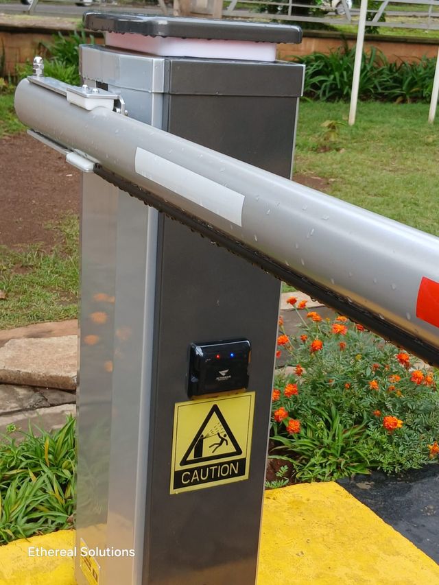 Close-up of an automatic boom barrier arm with a vehicle detector sensor mounted on the housing