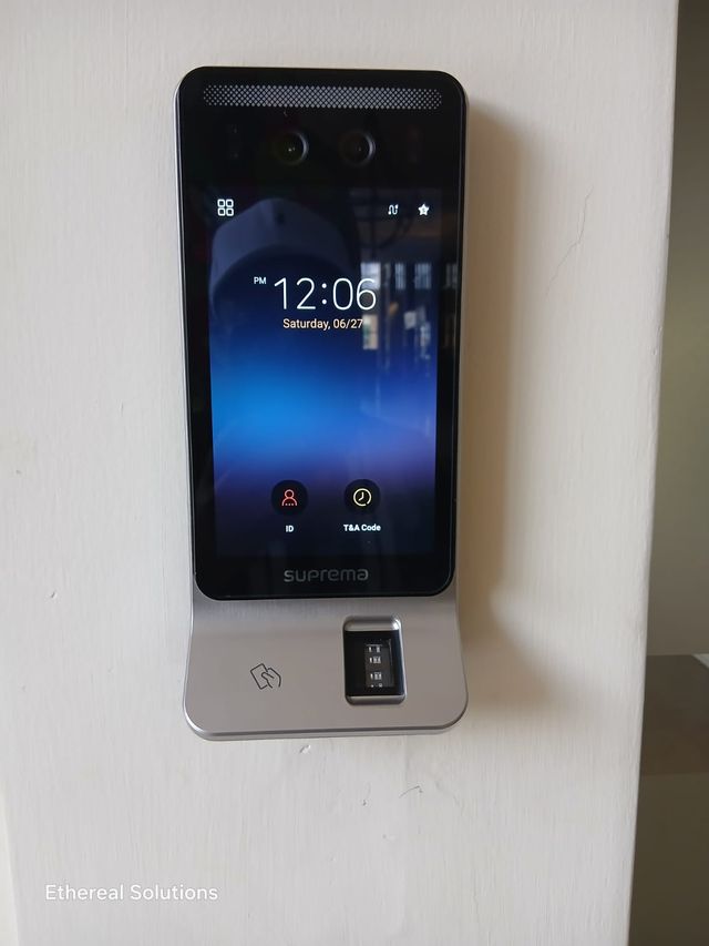 Suprema biometric time and attendance terminal mounted on an office wall showing the clock screen