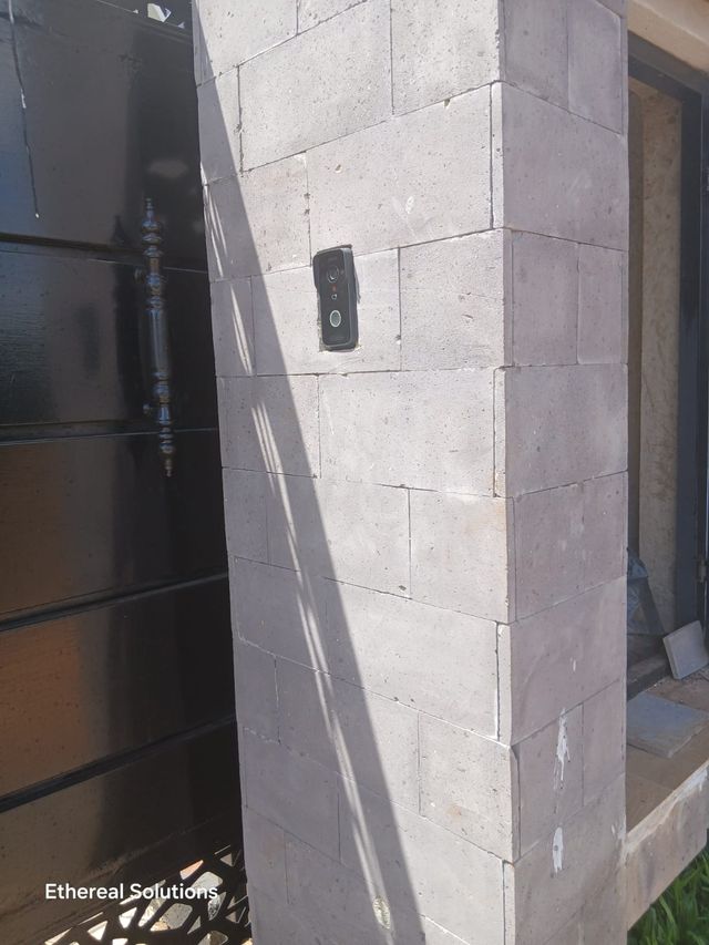 Video doorbell mounted at head height on a stone gate pillar beside a black steel gate