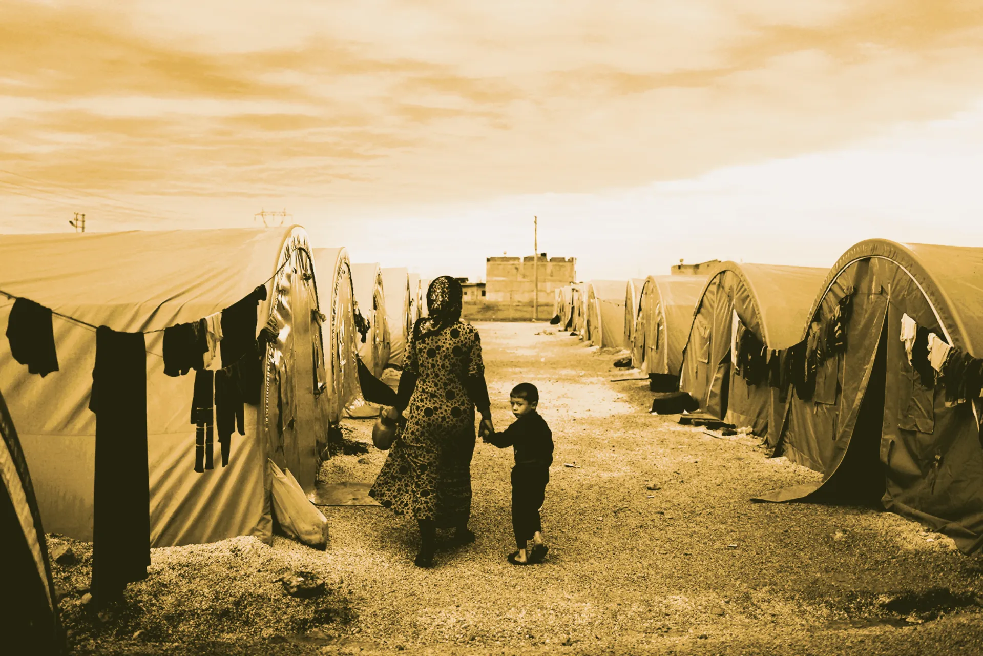 A mother and a child walking on a road amid tents
