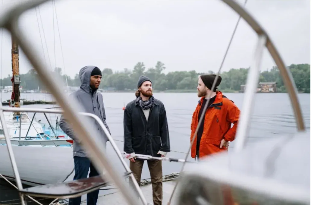 Three sailors chatting on a pontoon, seen from the helm of a sailboat