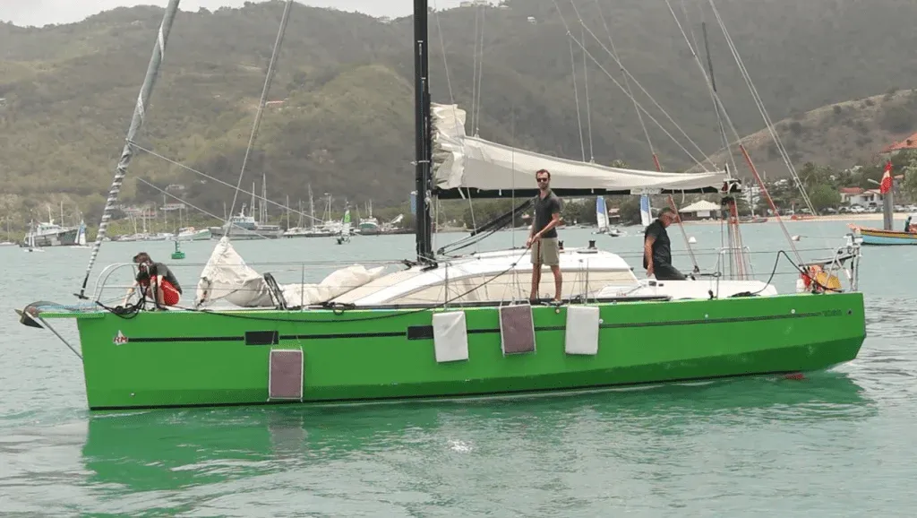Green-hulled sailboat at anchor in a bay, with the crew on deck