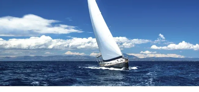 Sailboat heeling under mainsail and genoa off a coastline
