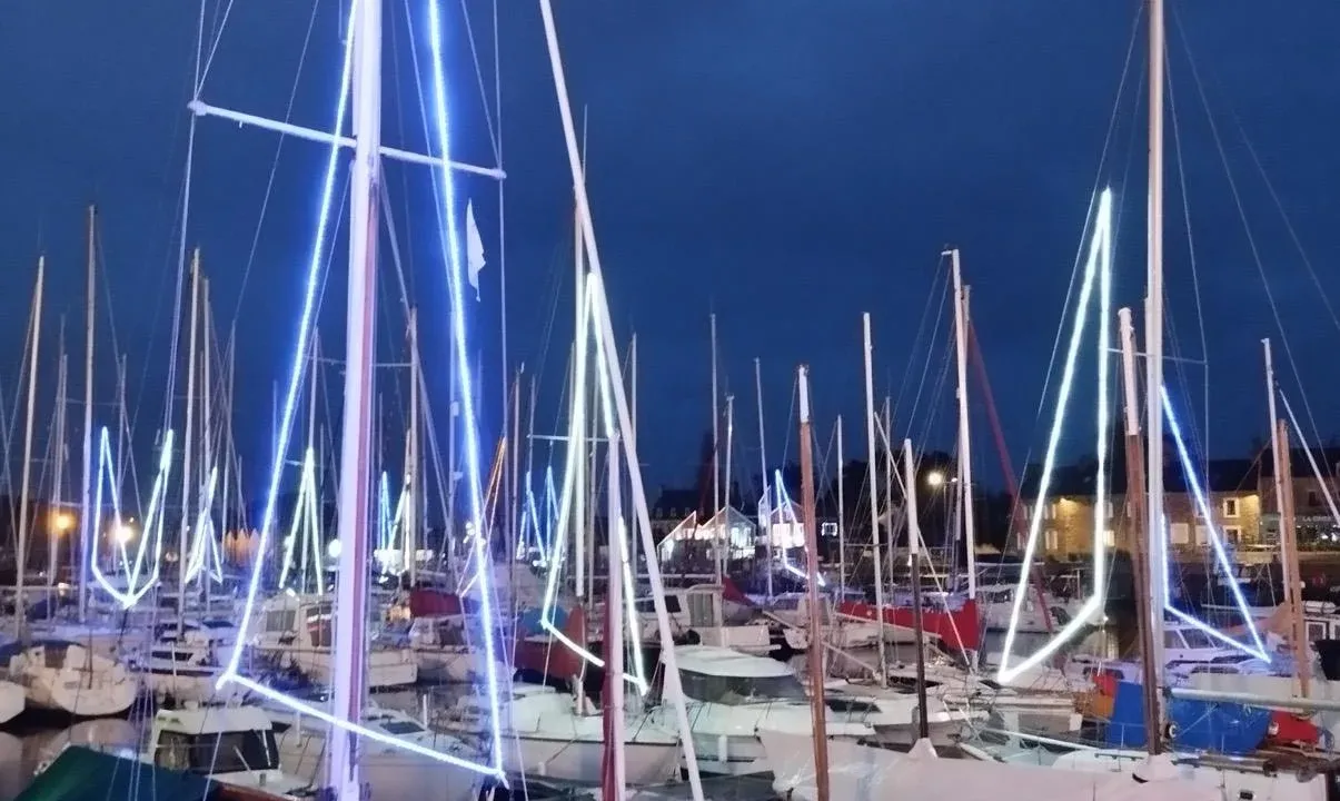 Sailboat masts lit up with string lights in a harbour at night