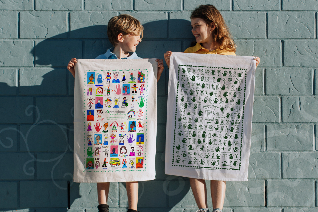 Children holding up personalised Expressions Fundraising tea towels featuring student artwork