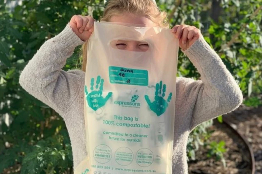 Child holding an eco-friendly, recyclable delivery bag from Expressions Fundraising with green handprints and sustainability message.