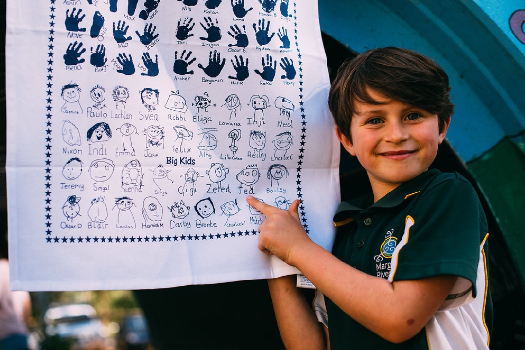 Two school children drying dishes with custom-printed tea towels featuring self-portraits, part of an eco-friendly school fundraising activity.