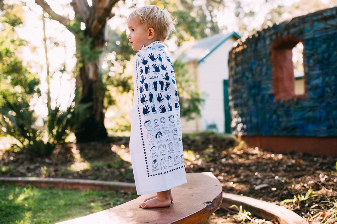 Young child proudly wearing a custom printed tea towel featuring handprints and drawings